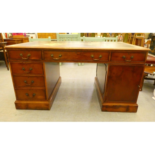 221 - A 20thC yewwood partner's desk with an arrangement of cupboard doors and drawers, on a plinth  ... 