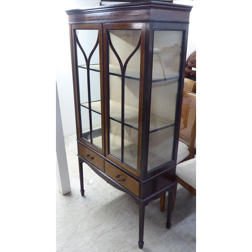 42 - A 1930s mahogany finished display cabinet with a pair of glazed doors, over two in-line drawers, rai... 