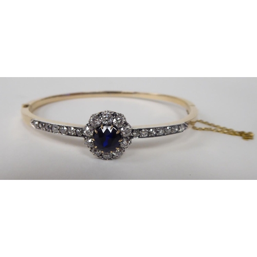 107 - A 15ct gold hinged bracelet, on a safety chain, claw set with a sapphire, surrounded by diamonds, be... 