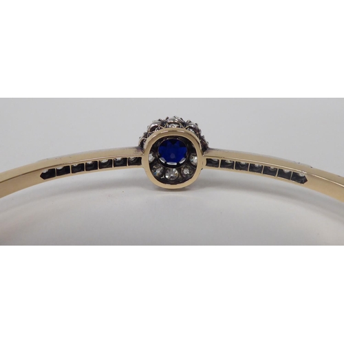 107 - A 15ct gold hinged bracelet, on a safety chain, claw set with a sapphire, surrounded by diamonds, be... 