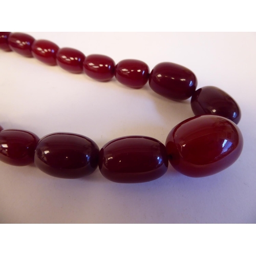 208 - A cherry coloured amber, oval graduated bead necklace with a pair of matching, oval bead pendant ear... 