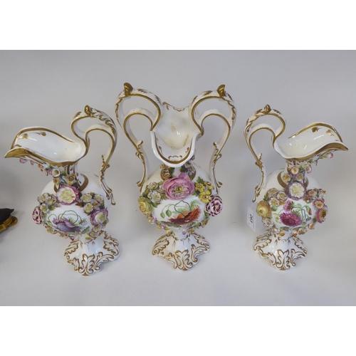 263 - A trio of late 19thC, possibly Coalbrookdale, china ewers of pedestal, bulbous form, painted, encrus... 