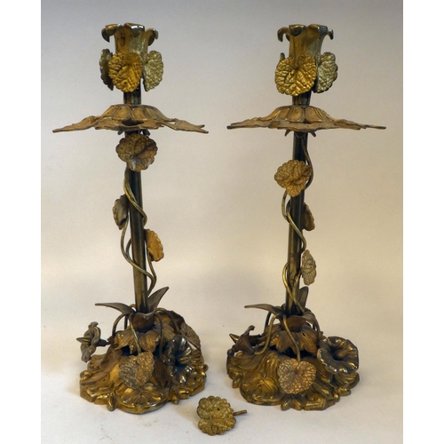 43 - A pair of late Victorian gilded metal, naturalistically formed candlesticks, adorned with trailing a... 