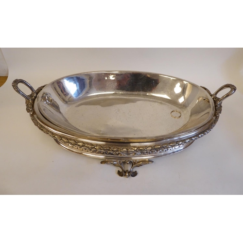 98 - An early 20thC silver plated, two-part serving dish of oval form, profusely cast with maskheads, pie... 