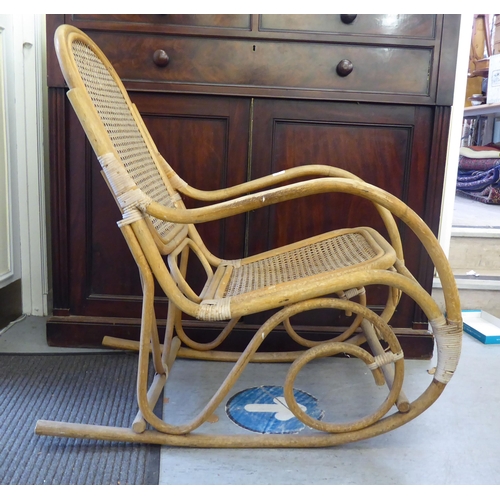 148 - A 1930s colonial design bamboo framed veranda rocking chair with a caned back and seat, raised on cu... 