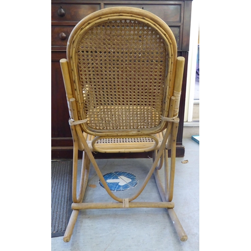 148 - A 1930s colonial design bamboo framed veranda rocking chair with a caned back and seat, raised on cu... 