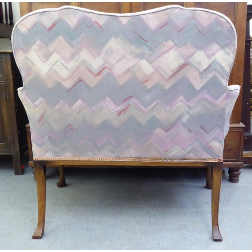 183 - A 1920s mahogany framed two person salon settee, upholstered in a multi-coloured fabric, raised on c... 