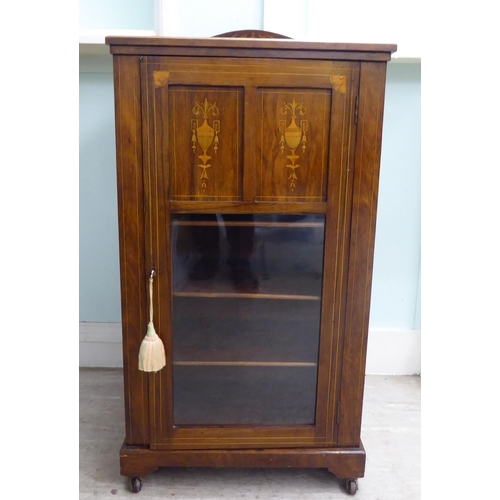 20 - An Edwardian string inlaid rosewood music cabinet with a panelled and glazed door, on a bracket plin... 