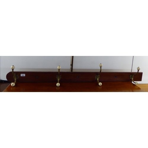 222 - A late Victorian hanging mahogany row of four decoratively cast brass hat and coat hooks with white ... 