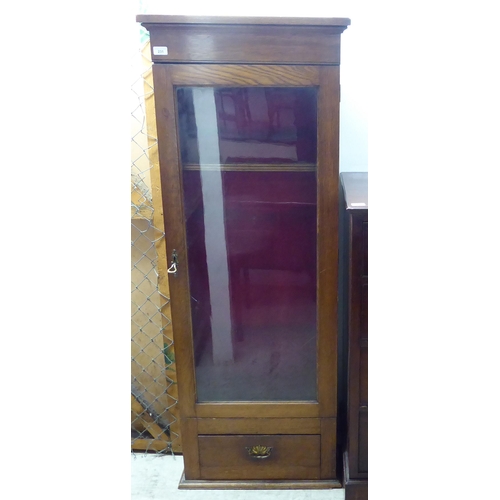 231 - An early 20thC oak gun cupboard with a full height glazed door, over a base drawer  62