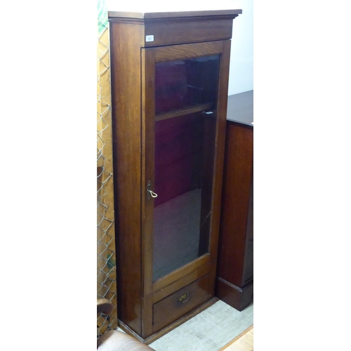 231 - An early 20thC oak gun cupboard with a full height glazed door, over a base drawer  62