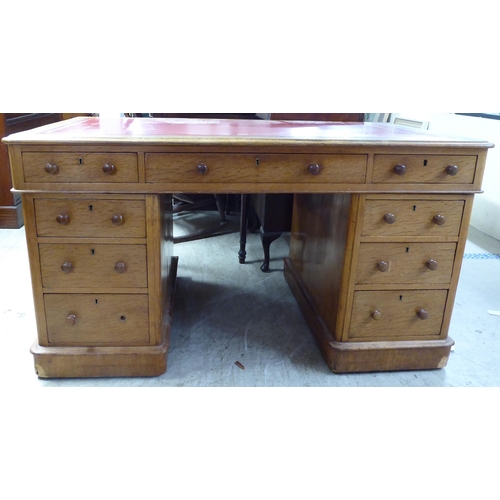 232 - An early 20thC honey coloured oak, twin pedestal, nine drawer desk with a tooled red hide scriber, o... 