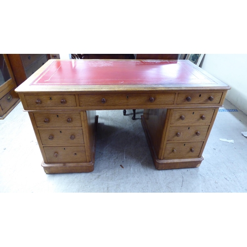 232 - An early 20thC honey coloured oak, twin pedestal, nine drawer desk with a tooled red hide scriber, o... 