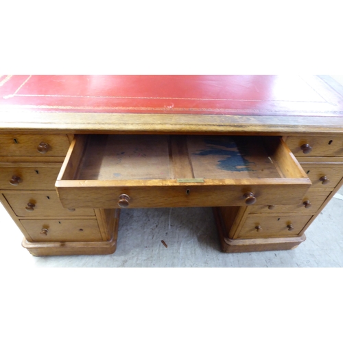 232 - An early 20thC honey coloured oak, twin pedestal, nine drawer desk with a tooled red hide scriber, o... 