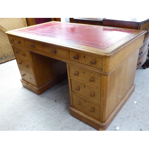 232 - An early 20thC honey coloured oak, twin pedestal, nine drawer desk with a tooled red hide scriber, o... 