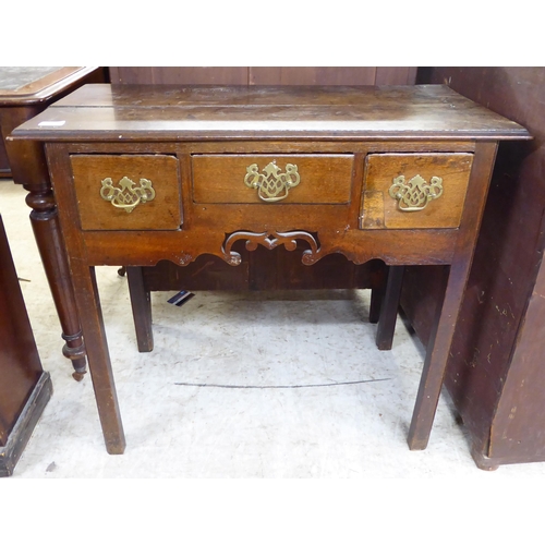 251 - A late 18thC oak lowboy, the planked top over three box drawers with brass handles on pierced backpl... 