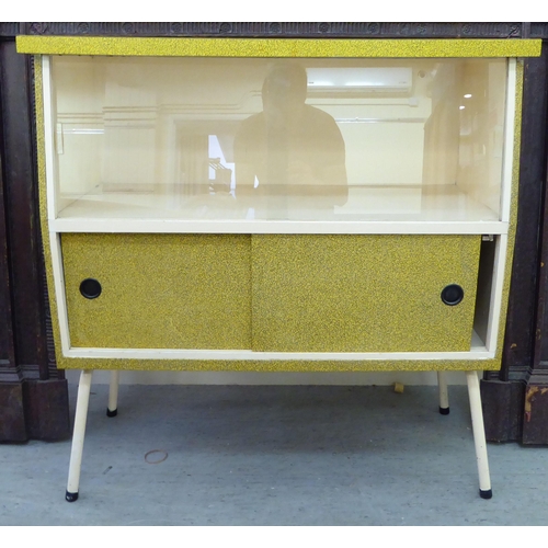 289 - A 1950s laminated cabinet with a pair of glazed sliding doors, raised on tubular legs  37