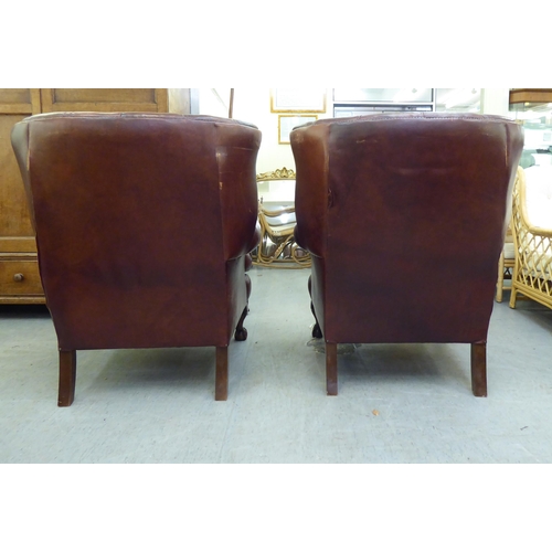 296 - A pair of modern Georgian reproduction red/brown hide upholstered, enclosed armchairs, raised on stu... 