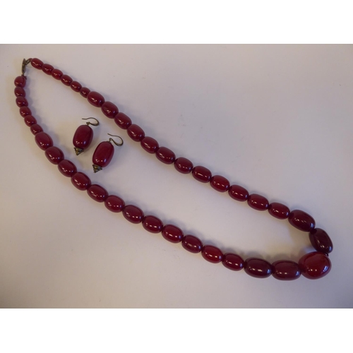 316 - A cherry coloured amber, oval graduated bead necklace with a pair of matching, oval bead pendant ear... 