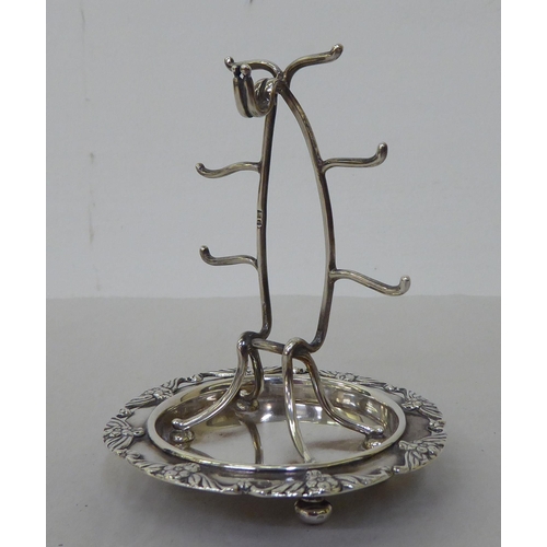 156 - A silver wire combination watch stand with ring hooks, on an integral saucer base, cast with flora, ... 