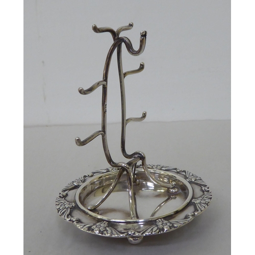 156 - A silver wire combination watch stand with ring hooks, on an integral saucer base, cast with flora, ... 