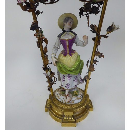 16 - An Austrian porcelain figure, painted in colours and wearing a summer dress, standing below a canopi... 