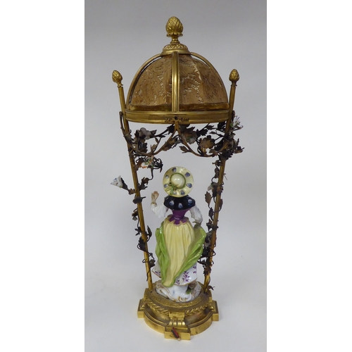 16 - An Austrian porcelain figure, painted in colours and wearing a summer dress, standing below a canopi... 