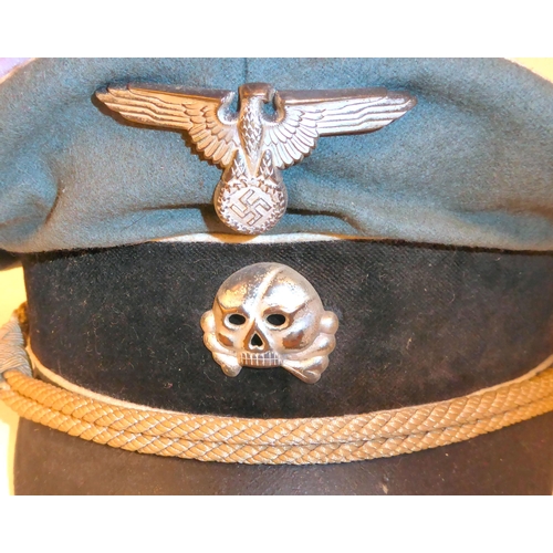 244 - A German SS green and black peaked cap with white piping, emblems and a cord(Please Note: this lot i... 