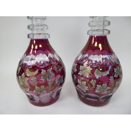 60 - A pair of 20thC part gilt painted, cranberry cut glass, bulbous decanters with triple ring necks and... 