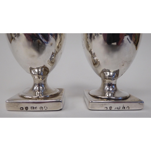 94 - A pair of Georgian silver, loaded pedestal, vase design pepper pots with detachable lids and finials... 