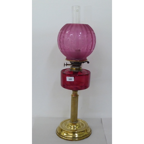 245 - A late Victorian brass oil lamp with a cranberry coloured glass reservoir, burner and reeded column,... 