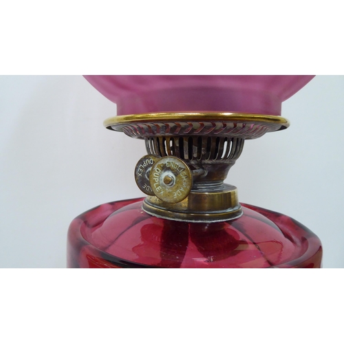 245 - A late Victorian brass oil lamp with a cranberry coloured glass reservoir, burner and reeded column,... 