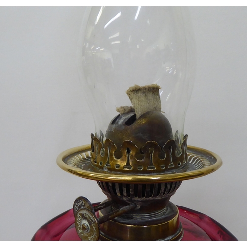 245 - A late Victorian brass oil lamp with a cranberry coloured glass reservoir, burner and reeded column,... 