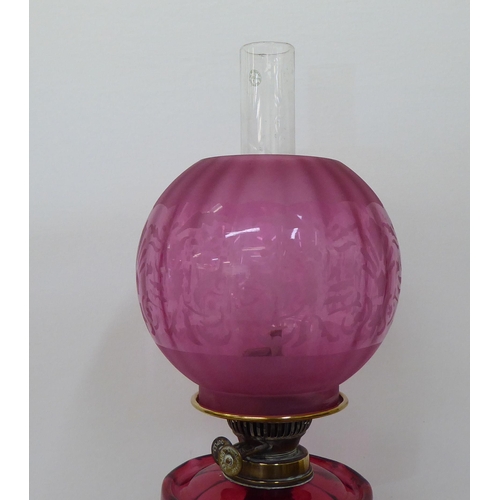 245 - A late Victorian brass oil lamp with a cranberry coloured glass reservoir, burner and reeded column,... 