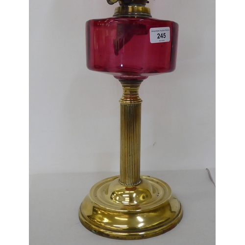 245 - A late Victorian brass oil lamp with a cranberry coloured glass reservoir, burner and reeded column,... 