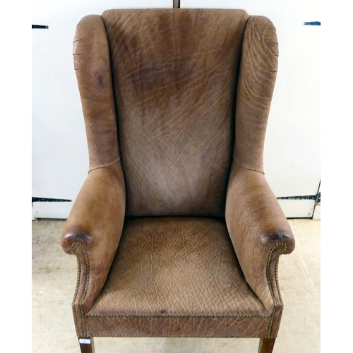 71 - An early 20thC Georgian reproduction of a stud upholstered, enclosed arm, high back chair, raised on... 