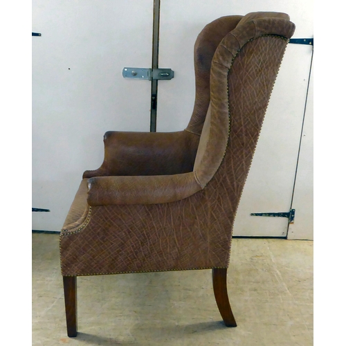 71 - An early 20thC Georgian reproduction of a stud upholstered, enclosed arm, high back chair, raised on... 