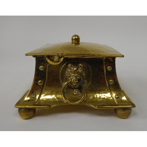 1 - An Arts & Crafts desktop beaten and rivetted brass inkwell of square, twin ring handled casket f... 