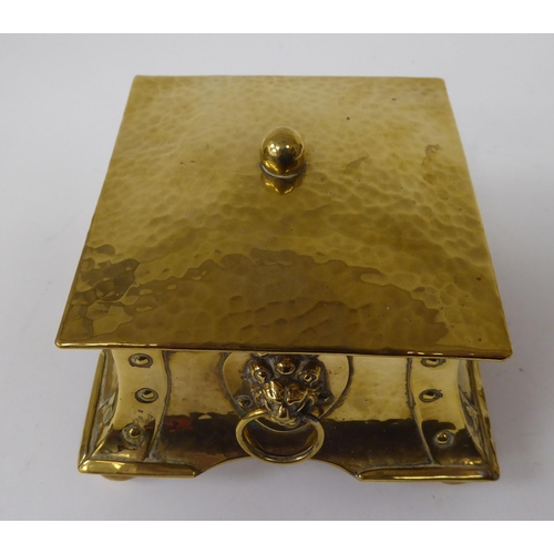 1 - An Arts & Crafts desktop beaten and rivetted brass inkwell of square, twin ring handled casket f... 