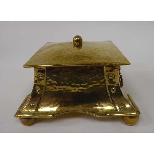 1 - An Arts & Crafts desktop beaten and rivetted brass inkwell of square, twin ring handled casket f... 