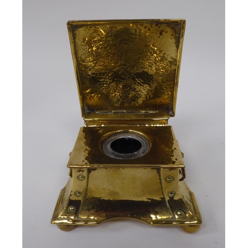 1 - An Arts & Crafts desktop beaten and rivetted brass inkwell of square, twin ring handled casket f... 