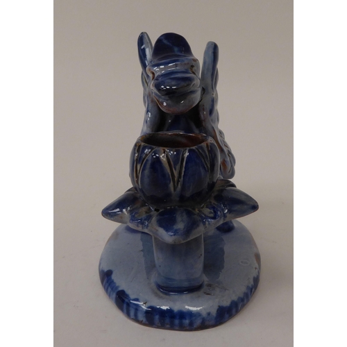 16 - An early 20thC Barum ware blue glazed pottery candle holder, fashioned as a griffin, on an oval base... 