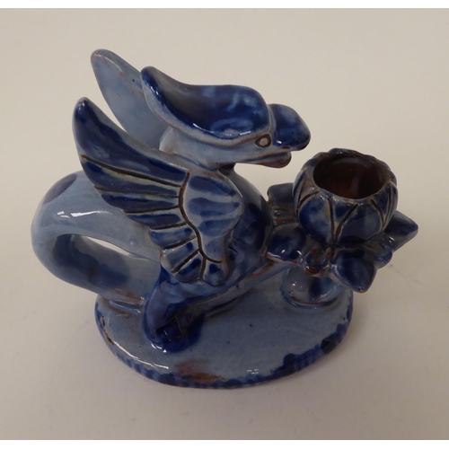 16 - An early 20thC Barum ware blue glazed pottery candle holder, fashioned as a griffin, on an oval base... 