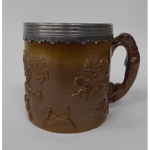 183 - A late 19thC brown stoneware mug with straight sides, a hunting dog handle, applied pewter rim and m... 