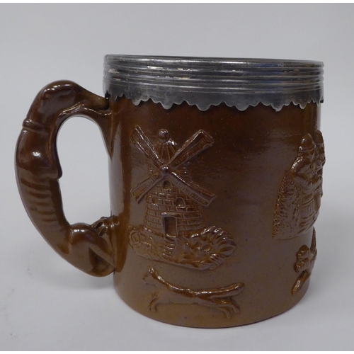 183 - A late 19thC brown stoneware mug with straight sides, a hunting dog handle, applied pewter rim and m... 