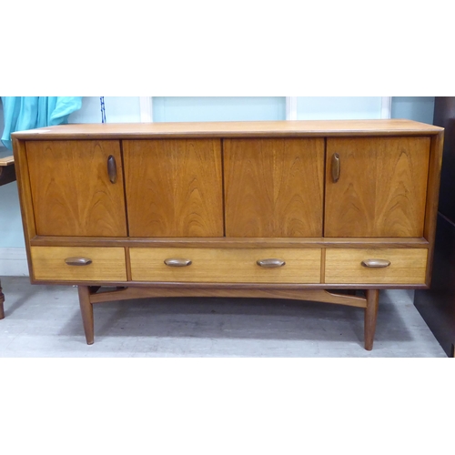 213 - A G-Plan teak sideboard with a pair of hinged doors, over three in-line drawers, raised on turned, t... 