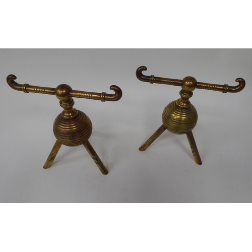 34 - A pair of late Victorian burnished brass hearth implement holders, on decoratively turned, tripod le... 