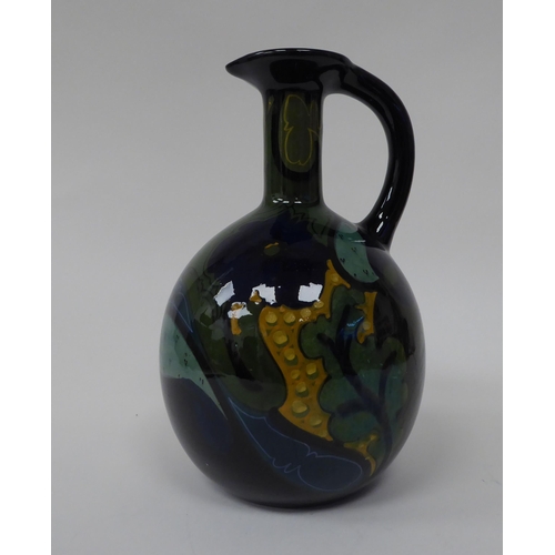 69 - A Gouda china spherical spirits bottle with a narrow neck, strap handle and pouring lip, decorated i... 