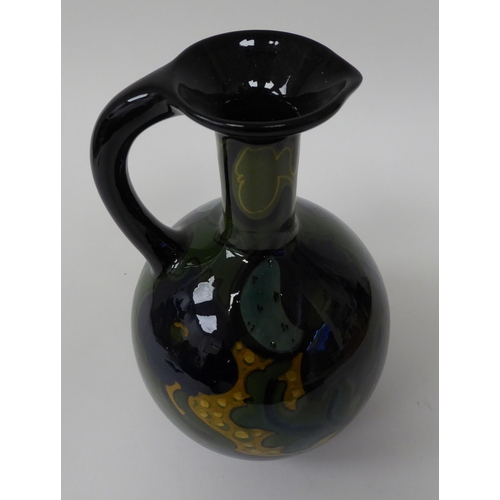 69 - A Gouda china spherical spirits bottle with a narrow neck, strap handle and pouring lip, decorated i... 