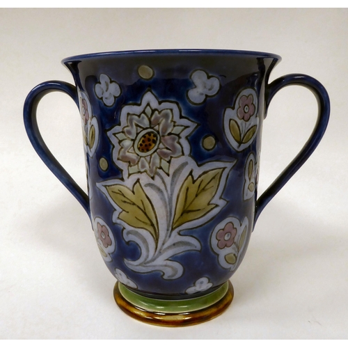 73 - An early 20thC Doulton stoneware twin handled loving cup, decorated with stylised floral designs, on... 